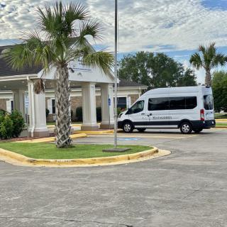 A white van parked outside a building with palm trees and a cloudy sky.
