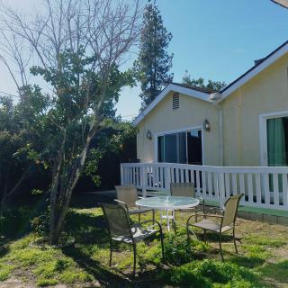 A cozy house with a garden patio featuring outdoor furniture and surrounding greenery on a sunny day.