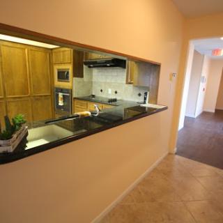 A modern open-concept kitchen featuring wood cabinets and a granite countertop, viewed from the hallway.