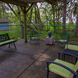 A cozy outdoor seating area under a wooden gazebo surrounded by lush greenery.
