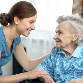A caregiver smiling and interacting with an elderly person.