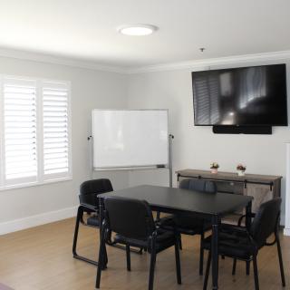 A well-lit conference room with a table and chairs, a whiteboard, and a television on the wall.