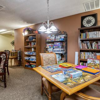 A cozy library interior with bookshelves and a reading table surrounded by chairs.