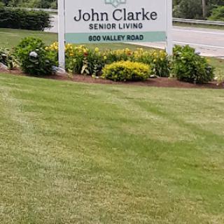 Welcome sign for John Clarke Senior Living along Red Valley Road, surrounded by well-maintained landscaping.