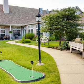 A peaceful garden setting featuring a mini golf course, benches, and a pathway leading to a building.