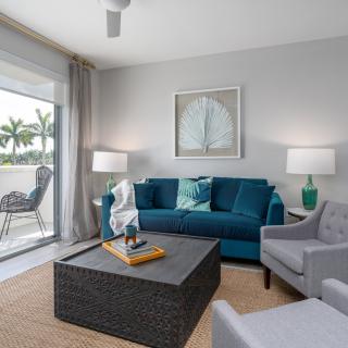 A modern living room with a blue sofa, gray armchair, and large windows providing natural light.
