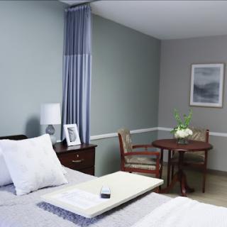 A cozy and modern bedroom featuring a neatly made bed, a wooden table with chairs, and soft color tones.