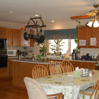 A cozy kitchen with wooden cabinets, a dining table, hanging pots, and indoor plants.