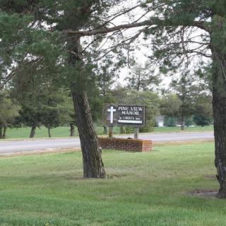 A church sign surrounded by trees and grass near a road.