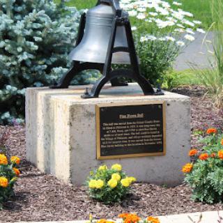 A memorial bell surrounded by a colorful garden.