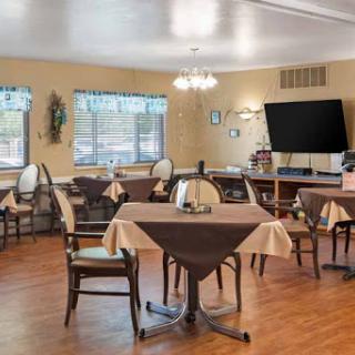 A cozy dining room setup with tables and chairs, featuring a television and ample natural light.
