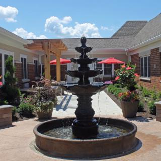 A serene courtyard featuring a multi-tiered fountain surrounded by greenery and patio seating.