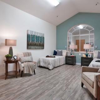 A well-furnished bedroom featuring two beds, comfortable chairs, modern lamps, artwork on the walls, and a stylish wooden floor.