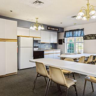 A community kitchen and dining area with multiple tables, chairs, and bright lighting.