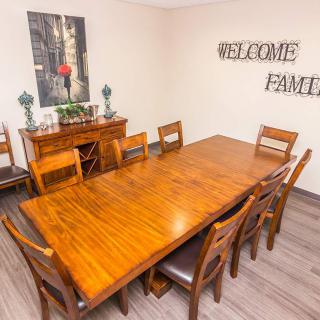 A dining room with a large wooden table and matching chairs, featuring a 'Welcome Family' sign on the wall.