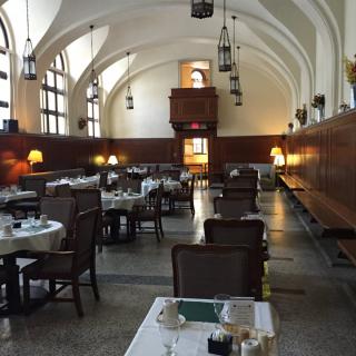 A spacious dining hall with elegantly set tables and an arched ceiling, softly lit by hanging lamps.