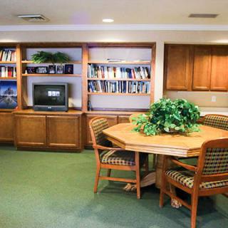 A cozy library room with bookshelves, a television, a round table surrounded by chairs, and an indoor plant.