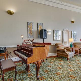 A cozy living room featuring a grand piano, upholstered armchairs, and elegant decor.