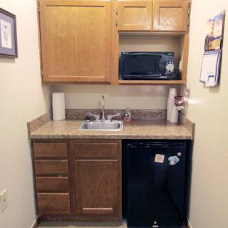 A compact kitchenette with wooden cabinets, a microwave, sink, and a small refrigerator.