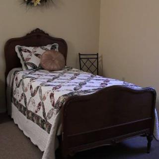 A cozy bedroom with a single bed featuring traditional wooden furniture and a quilted coverlet.