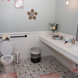 A well-decorated bathroom with a patterned tile floor, featuring a toilet, sink, mirror, and floral decorations.