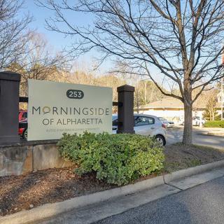 Entrance sign for Morningside of Bloomington with surrounding landscape and parked cars.
