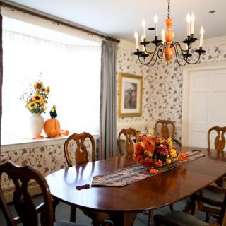 A cozy dining room with elegant decor, featuring a wooden table set for autumn with pumpkins and flowers.