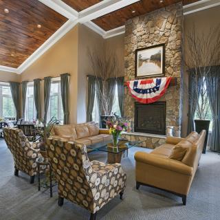 A spacious living room featuring a stone fireplace, elegant sofa set, and large windows with decorative curtains.