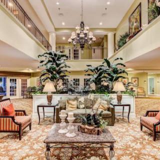 A luxurious lobby interior with elegant furniture, a central chandelier, and large decorative plants.