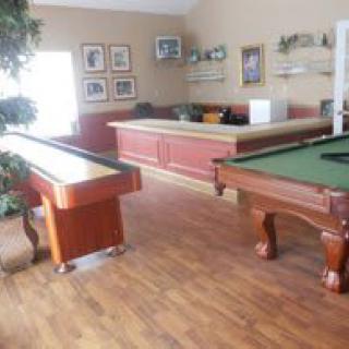 A cozy game room with a billiard table and shuffleboard setup, featuring hardwood flooring and casual seating.