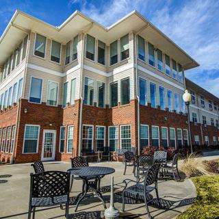 A modern three-story building with large windows and outdoor seating under a clear blue sky.
