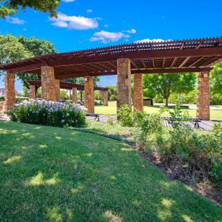 A beautiful park with a pergola surrounded by lush greenery on a sunny day.