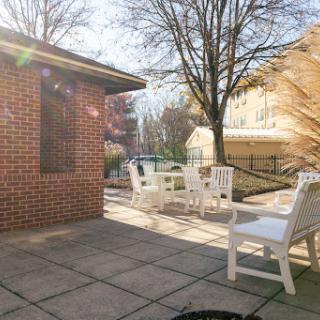 A sunny patio area featuring white outdoor furniture surrounded by trees.