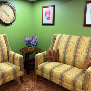 A cozy living room with two patterned sofas, a side table with a flower vase, and artwork on green walls.