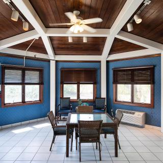 A spacious dining room with a wooden ceiling and large windows, furnished with a glass table and chairs.