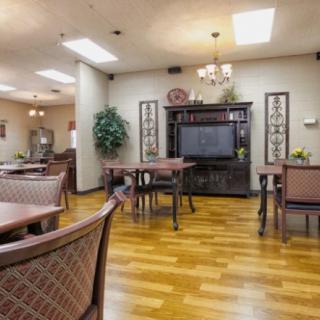 A cozy dining area with wooden floors, tables, chairs, and a television in the background.