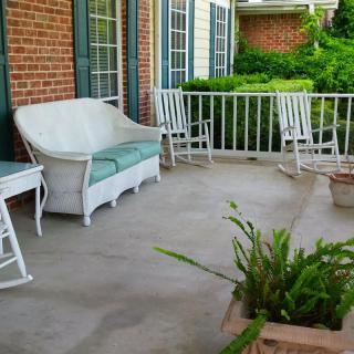 A cozy porch featuring white outdoor furniture, including a sofa and rocking chairs, with plants adding a touch of greenery.