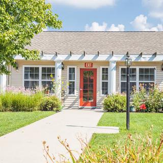 A charming house with a red door, surrounded by a well-maintained garden on a sunny day.