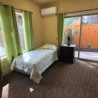 A cozy bedroom with a single bed, green curtains, and a sliding glass door leading outside.