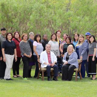 A group of people posing for a photo outdoors in a grassy area with trees in the background.