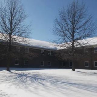 A snow-covered landscape with trees and a building under a clear blue sky.
