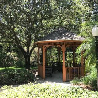 A tranquil garden scene featuring a wooden gazebo surrounded by lush greenery and trees.