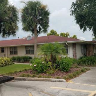 A single-story house with a red roof, surrounded by palm trees and a well-maintained garden.