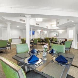 A modern dining room with neatly arranged tables and chairs, featuring blue napkins and floral centerpieces.