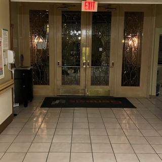 The image shows a tiled lobby entrance with double glass doors and an exit sign above.