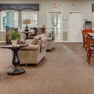 A spacious living room area with sofas, chairs, and a table, featuring carpeted flooring and large windows.