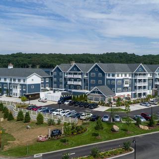 Aerial view of a modern residential building complex with a parking lot and landscaped surroundings.