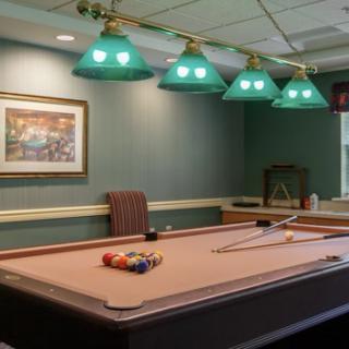 A cozy game room featuring a well-lit pool table and green lamps.