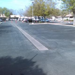 A spacious, empty parking lot during the day, lined with trees and a few parked vehicles.