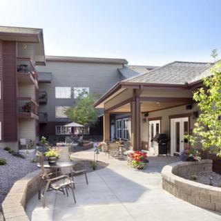 A modern residential building with a landscaped patio featuring outdoor seating and tables on a sunny day.